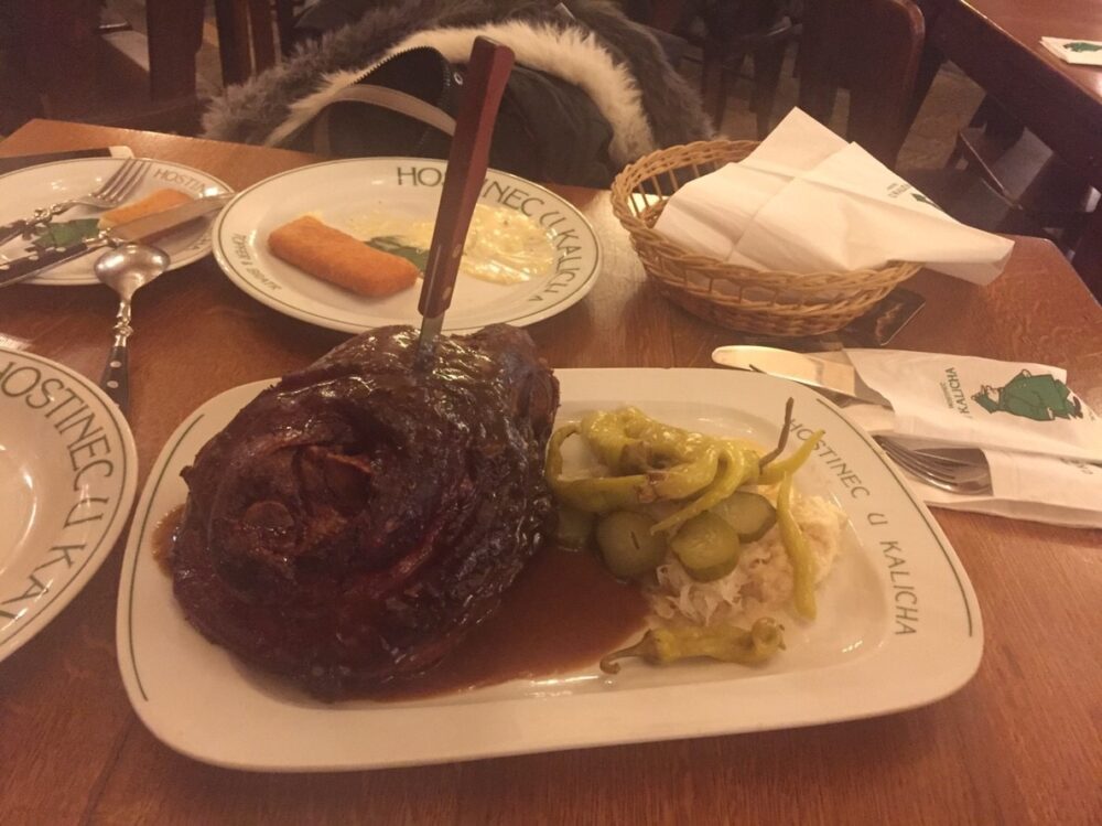 プラハの老舗ビアホール「ホスチネツ・ウ・カリハ」で提供された、ナイフが垂直に突き刺さった巨大な豚のひざ肉のロースト（ヴェプロヴェー・コレノ）。皮がこんがりと焼かれている様子