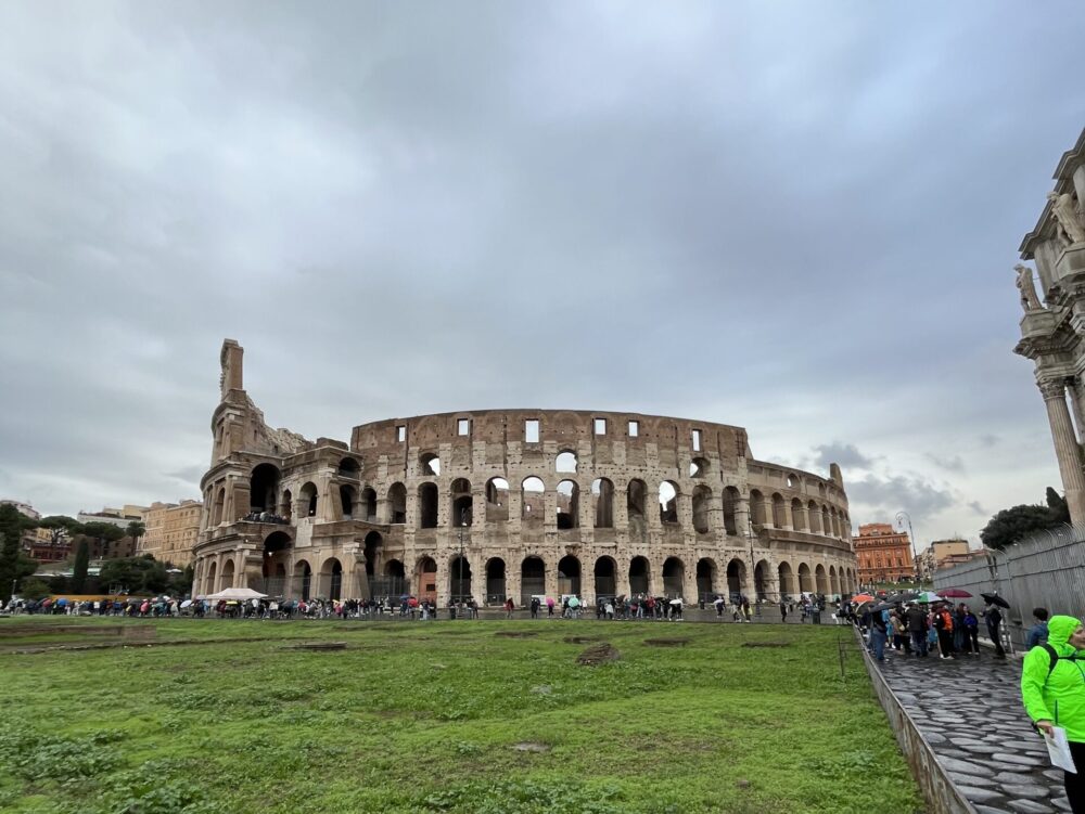 青空の下に広がる巨大なコロッセオの全景と緑の芝生
