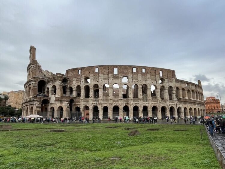 青空の下に広がる巨大なコロッセオの全景と緑の芝生