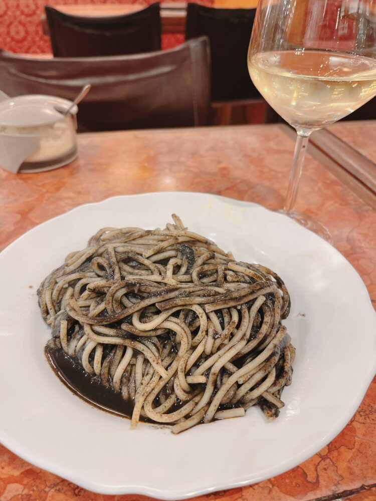 ヴェネチアの名物のイカスミパスタと冷えた白ワインの豪華なランチ