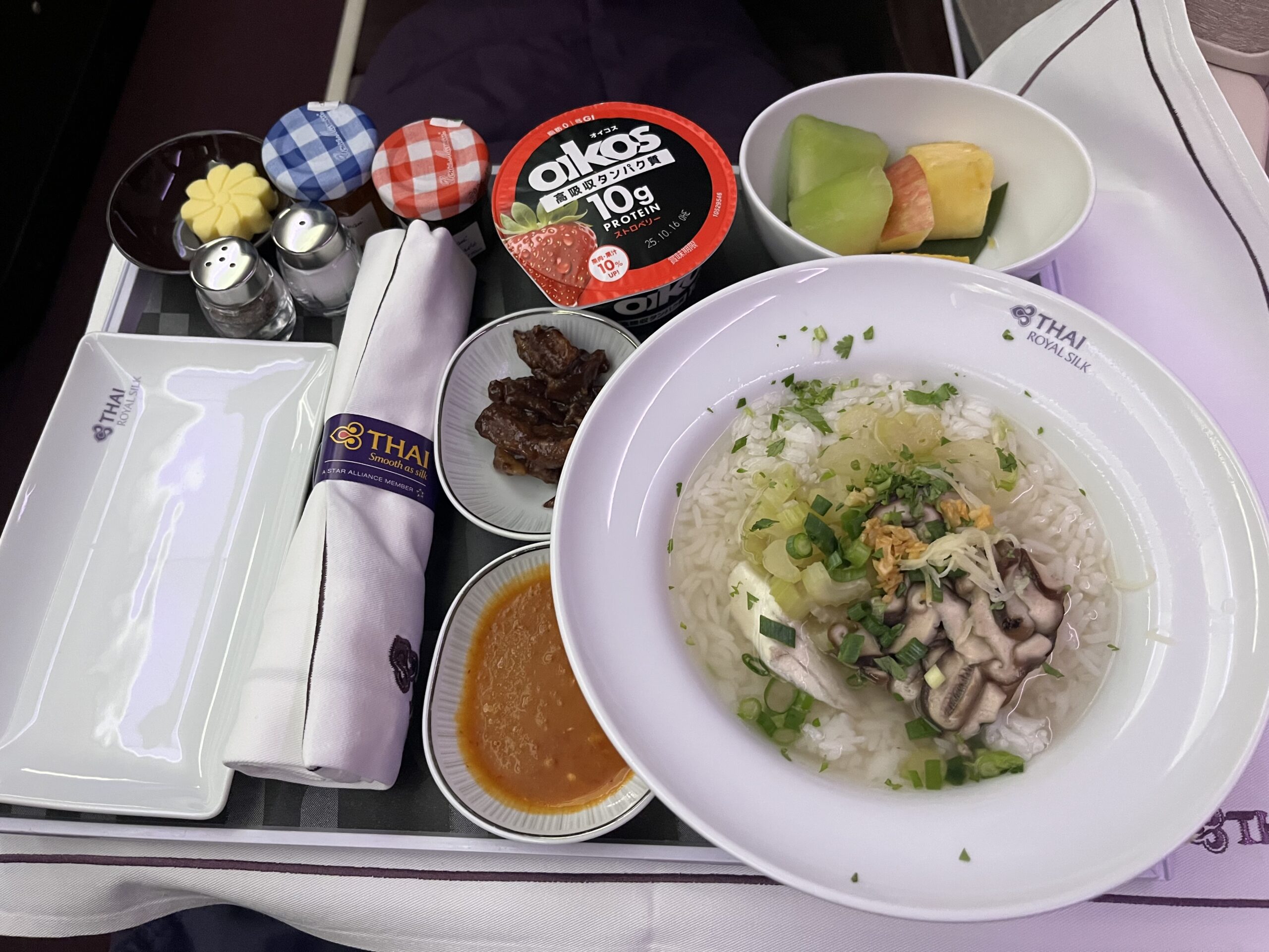 タイ航空ビジネスクラスの朝食。スズキの切り身が入ったタイ風のお粥と、豚ひき肉の甘醤油炒めが並ぶ豪華なトレイ。
